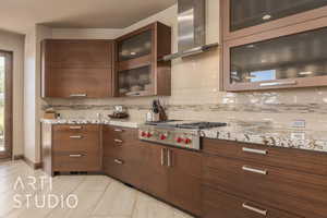 Kitchen with stainless steel gas cooktop, light stone countertops, wall chimney range hood, and decorative backsplash