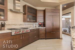 Kitchen with stainless steel gas cooktop, light stone counters, light tile patterned floors, and wall chimney range hood