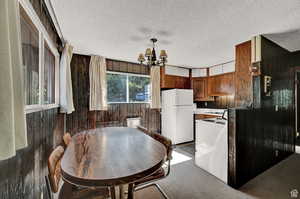 Kitchen with white appliances, wood walls, a notable chandelier, and a textured ceiling