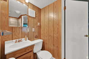 Bathroom with an enclosed shower, a textured ceiling, toilet, wood walls, and vanity