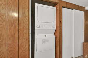 Clothes washing area featuring a textured ceiling, wood walls, and stacked washer / dryer