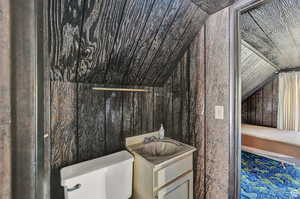 Bathroom with vanity, toilet, wooden walls, and vaulted ceiling