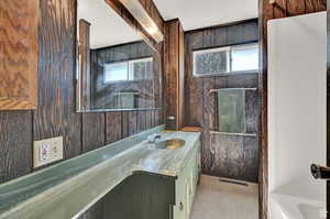 Bathroom with wooden walls, a bathing tub, a textured ceiling, and vanity