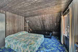 Unfurnished bedroom featuring carpet flooring, vaulted ceiling, wooden walls, and wooden ceiling