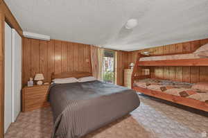 Carpeted bedroom featuring a textured ceiling and wood walls