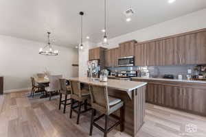 Kitchen with tasteful backsplash, stainless steel appliances, an inviting chandelier, an island with sink, and a breakfast bar