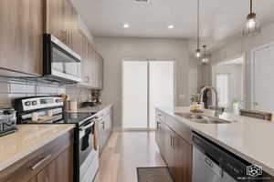 Kitchen featuring hanging light fixtures, light wood-type flooring, appliances with stainless steel finishes, sink, and decorative backsplash