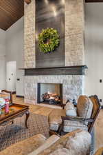 Living room featuring hardwood / wood-style floors, high vaulted ceiling, a stone fireplace, and wooden ceiling