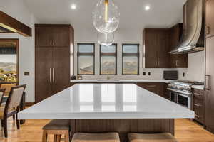 Kitchen with a center island, backsplash, wall chimney range hood, high end stainless steel range oven, and decorative light fixtures