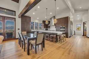 Dining area with beamed ceiling, light wood-type flooring, and high vaulted ceiling