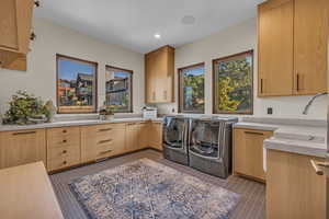 Clothes washing area with washing machine and clothes dryer, tile patterned floors, sink, and cabinets