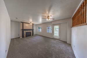 Unfurnished living room featuring carpet flooring, ceiling fan, a tiled fireplace, and a textured ceiling