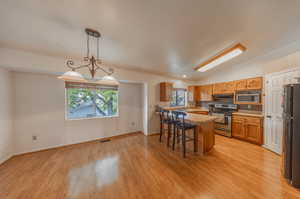 Kitchen with light hardwood / wood-style flooring, appliances with stainless steel finishes, a kitchen breakfast bar, and sink