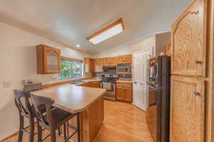 Kitchen featuring light wood-type flooring, appliances with stainless steel finishes, lofted ceiling, kitchen peninsula, and a kitchen breakfast bar