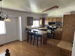 Kitchen featuring hanging light fixtures, kitchen peninsula, dark wood-type flooring, stainless steel appliances, and a kitchen bar