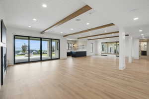 Unfurnished living room featuring recessed lighting, baseboards, light wood finished floors, beamed ceiling, and healthy amount of natural light