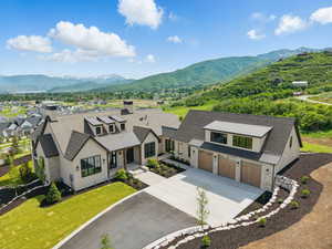 View of front facade with a standing seam roof, driveway, an attached garage, stone siding, and roof with shingles