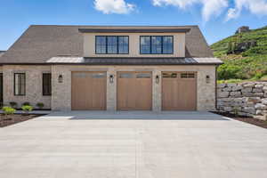 View of front facade featuring a standing seam roof, stone siding, driveway, and a garage