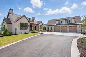 Modern farmhouse with a chimney, asphalt driveway, a standing seam roof, a front lawn, and a shingled roof