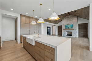 Kitchen with a sink, light wood-style flooring, baseboards, vaulted ceiling, and wood ceiling