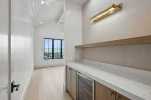 Bar area featuring beverage cooler, light wood-type flooring, recessed lighting, baseboards, and high vaulted ceiling