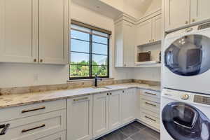 Washroom featuring stacked washing maching and dryer, cabinets, sink, and dark tile patterned floors