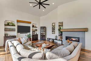 Living room featuring built in shelves, ceiling fan, hardwood / wood-style floors, and high vaulted ceiling