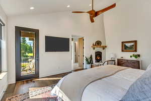 Master Bedroom featuring hardwood / wood-style flooring, a large fireplace, ceiling fan, access to outside, and high vaulted ceiling