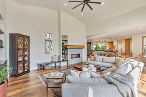 Living room with high vaulted ceiling, ceiling fan, and light hardwood / wood-style floors