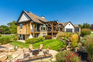 Back of property with a yard, a garage, a fire pit, a patio, and a balcony