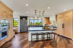 Kitchen with stainless steel appliances, dark hardwood / wood-style flooring, light brown cabinetry, a center island, and a breakfast bar