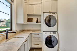 Clothes washing area featuring cabinets, sink, and stacked washer / dryer