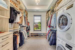 Master Walk in closet featuring stacked washer and clothes dryer, light carpet, and a tray ceiling