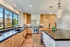 Kitchen with light hardwood / wood-style flooring, hanging light fixtures, sink, light brown cabinets, and high end range