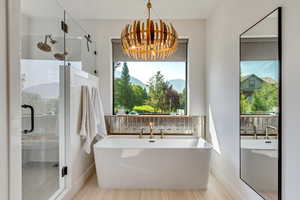 Master Bathroom with shower with separate bathtub and a notable chandelier