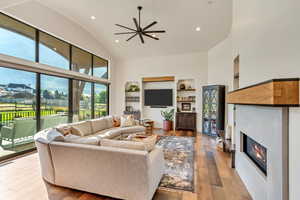 Living room with built in features, ceiling fan, hardwood / wood-style floors, and high vaulted ceiling