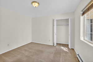 Unfurnished bedroom with a baseboard radiator, light carpet, and a closet
