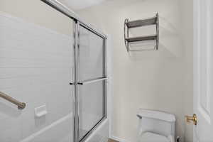 Bathroom featuring toilet and bath / shower combo with glass door