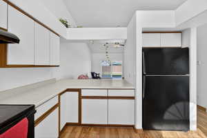 Two tone kitchen with two tone cabinets, black appliances, light countertops, light wood-type flooring, and a ceiling fan