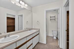 Full bathroom with double vanity, a spacious closet, and light carpet