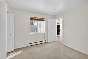 Unfurnished bedroom featuring a baseboard radiator and light carpet