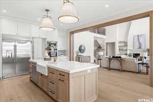 Kitchen with built in appliances, a fireplace, a center island with sink, light stone counters, and light wood-type flooring