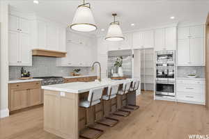 Kitchen featuring built in appliances, light hardwood / wood-style floors, a center island with sink, and white cabinets