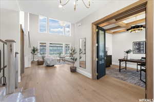 Interior space featuring light wood-type flooring, a chandelier, coffered ceiling, a high ceiling, and beam ceiling