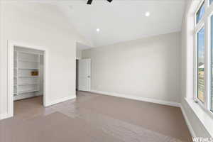 Unfurnished bedroom with light colored carpet, ceiling fan, a closet, a spacious closet, and high vaulted ceiling