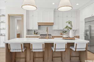 Kitchen featuring light wood-type flooring, light stone countertops, stainless steel built in fridge, and a kitchen island with sink