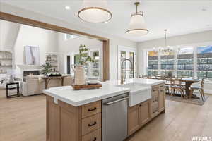 Kitchen featuring a large fireplace, light hardwood / wood-style floors, a kitchen island with sink, and stainless steel dishwasher