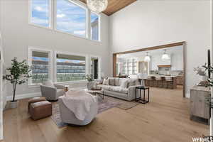 Living room with a wealth of natural light, light hardwood / wood-style flooring, a notable chandelier, and high vaulted ceiling