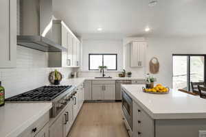 Kitchen featuring light wood-type flooring, stainless steel appliances, sink, wall chimney exhaust hood, and tasteful backsplash