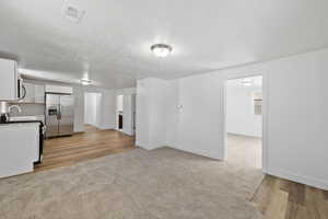 Kitchen with a textured ceiling, light wood-type flooring, appliances with stainless steel finishes, and white cabinetry